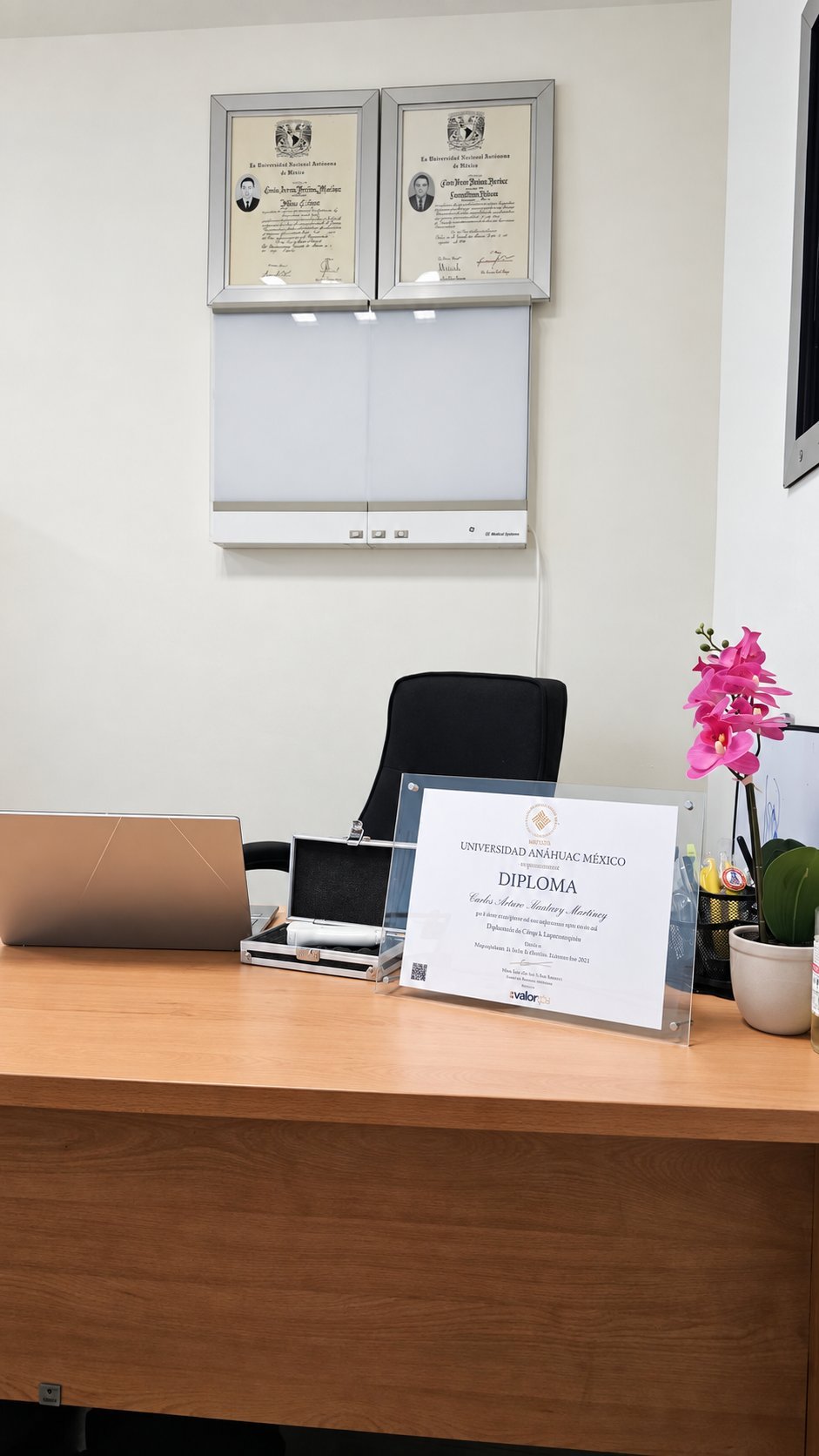 Consultorio con escritorio, diplomas enmarcados en la pared y orquídea