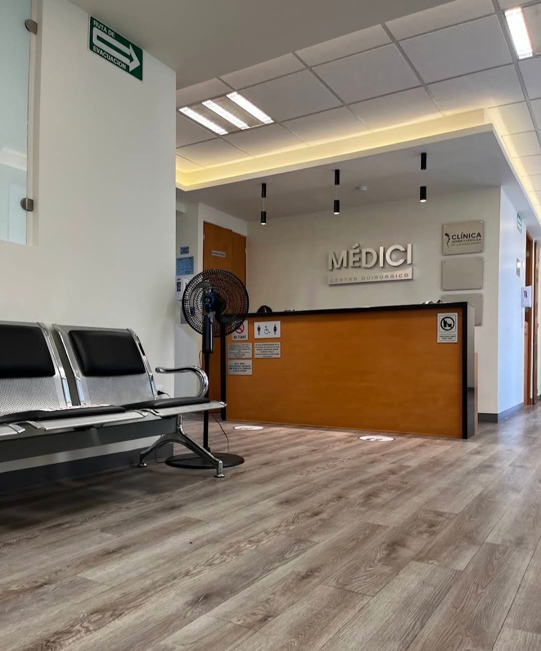 Recepción de la clínica con mostrador naranja, sillas de espera y rótulo MEDICI